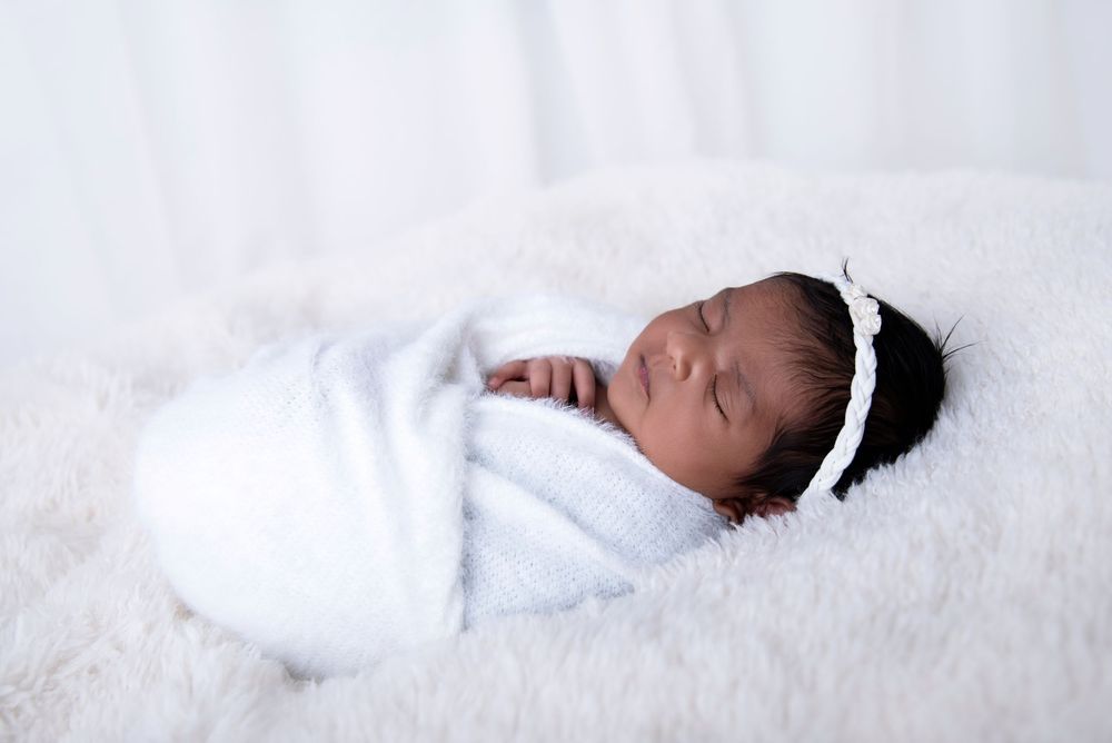 sleeping baby girl wrapped in whit on a white blanket and white backdrop in her Gold Coast newborn photography session