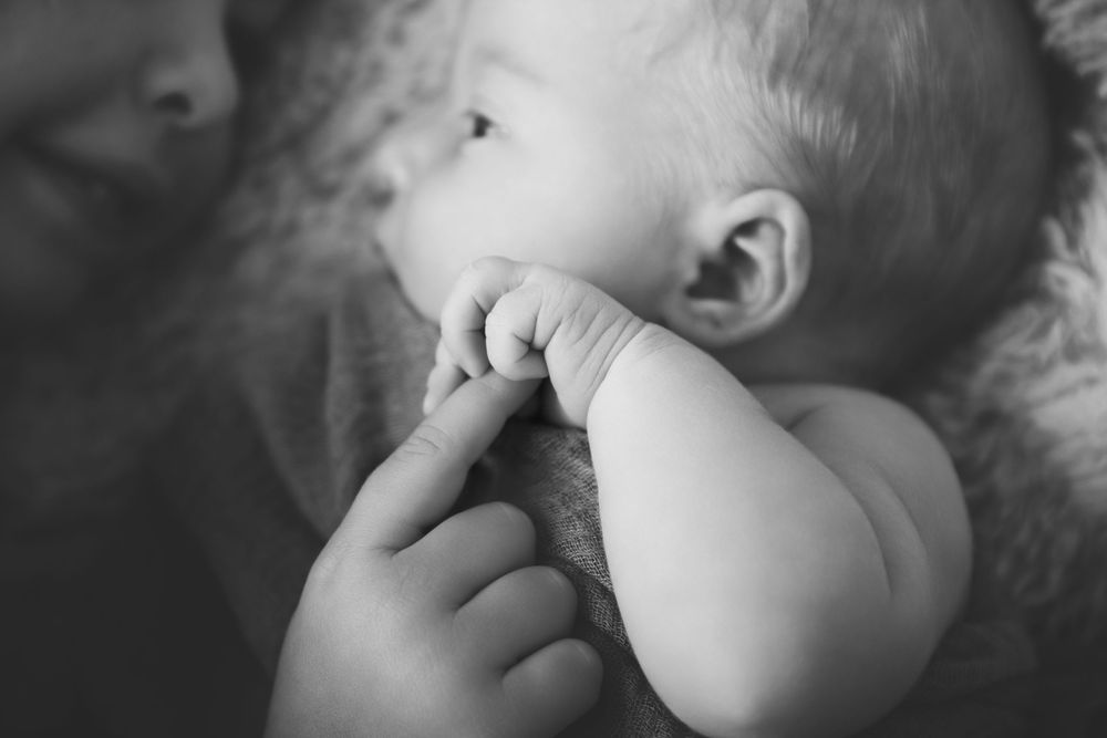 newborn baby girl holding her big sisters finger at her newborn photography session