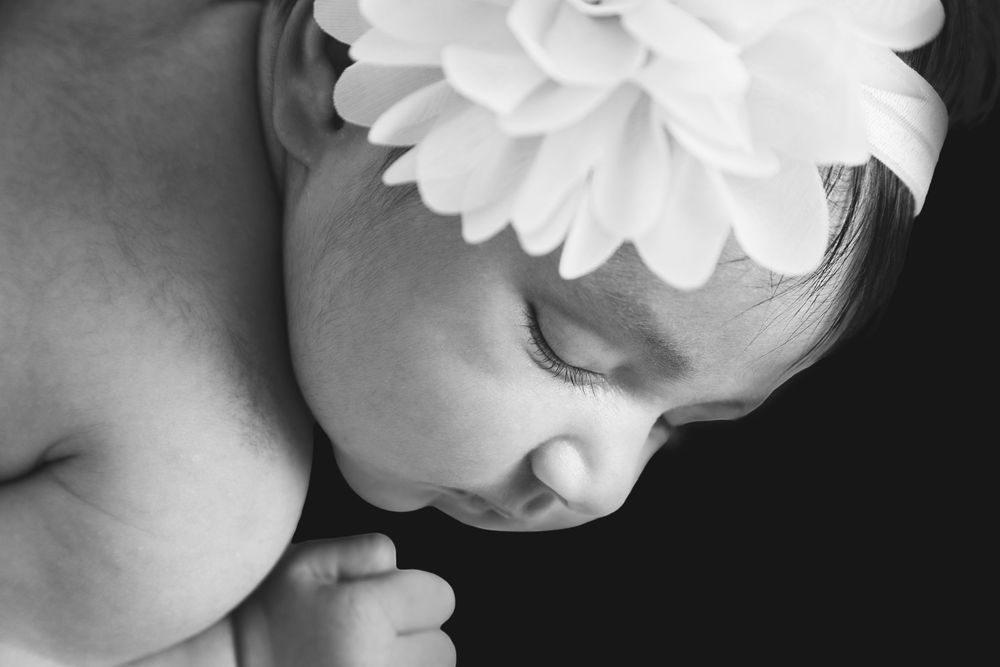 close up profile black and white photo of a baby girl with a large white flower headband on showing he little face