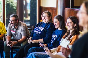 Group of smiling college students sitting together in casual discussion during a campus event.