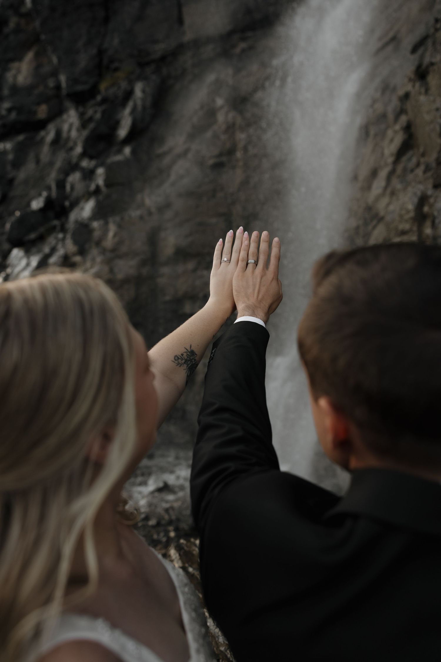 Bride and groom walk on a mountain road in Glacier National Park, wedding dress flowing, dramatic peaks in background.