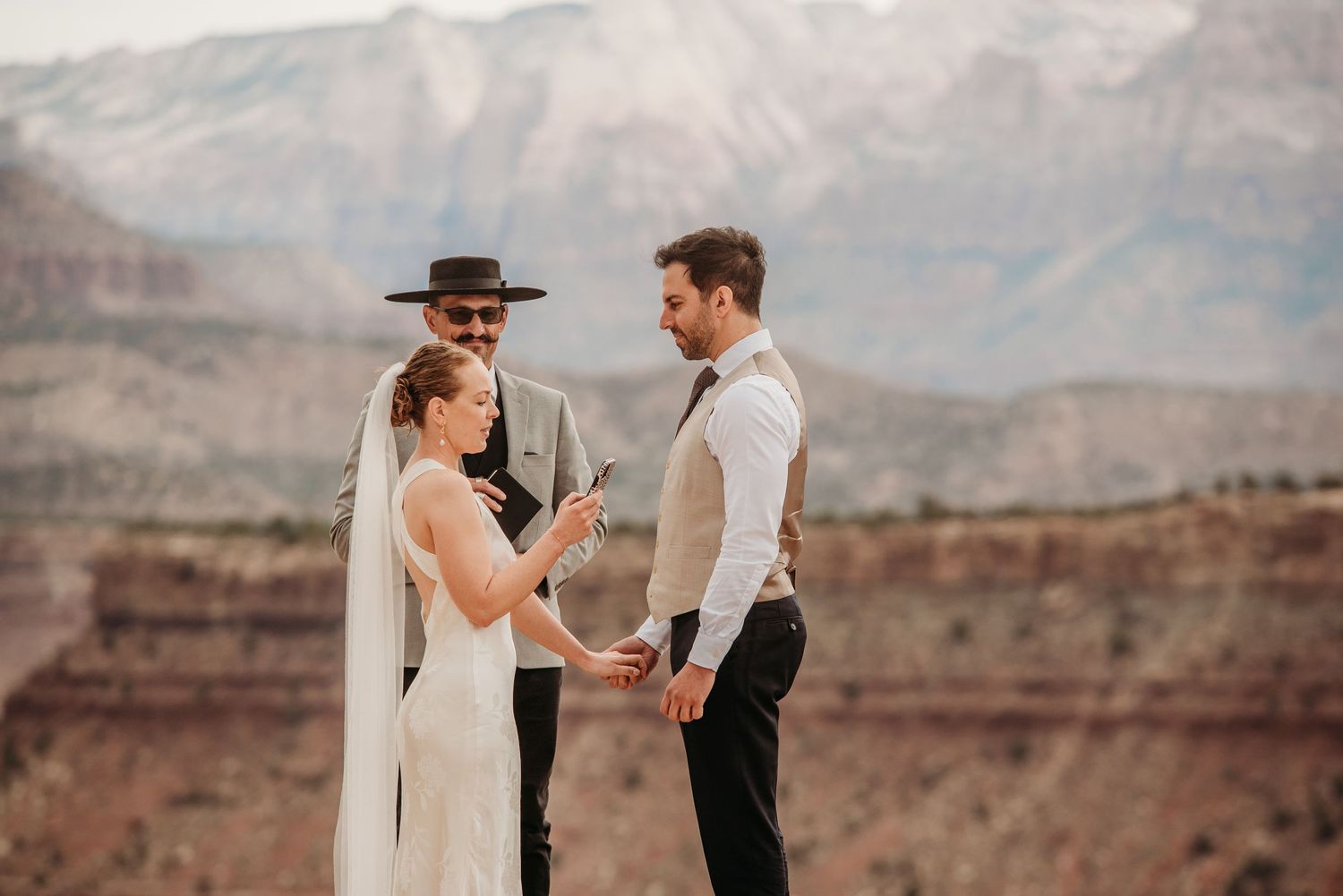 Bride and groom exchange vows at a desert elopement ceremony with stunning red rock mountains in the background.