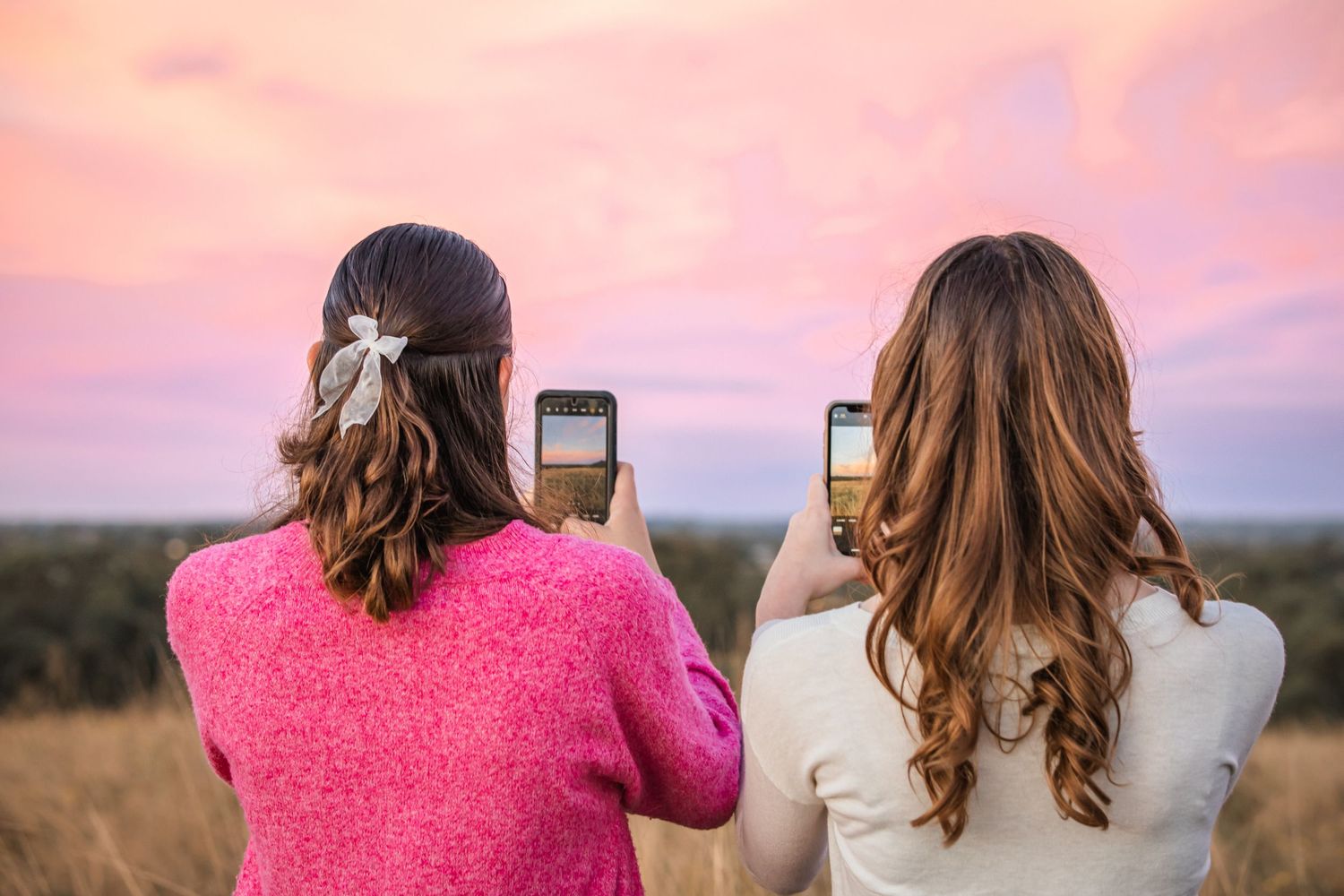 Two women photographing a vibrant pink and purple sunset sky with smartphones in an open field at Rouse Hill Regional Park during blue hour.