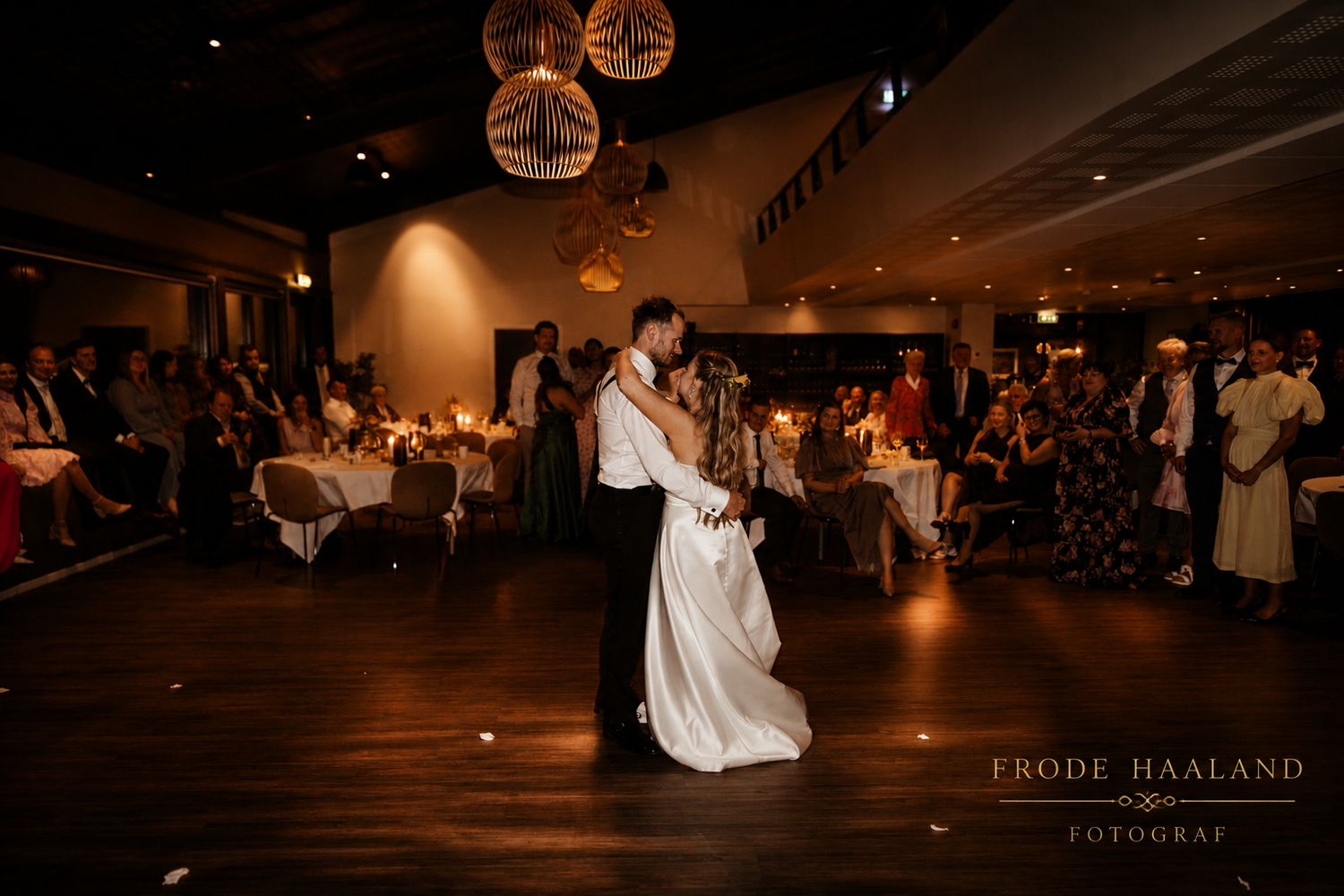 Couple shares their first dance at a romantic wedding reception with warm lighting and guests watching.