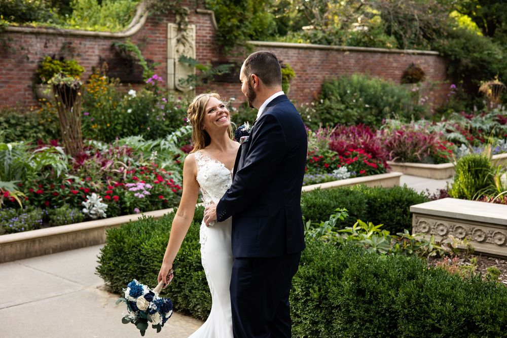 Bride and groom share a romantic moment in a lush garden, bride holding a blue and white bouquet in a white gown.