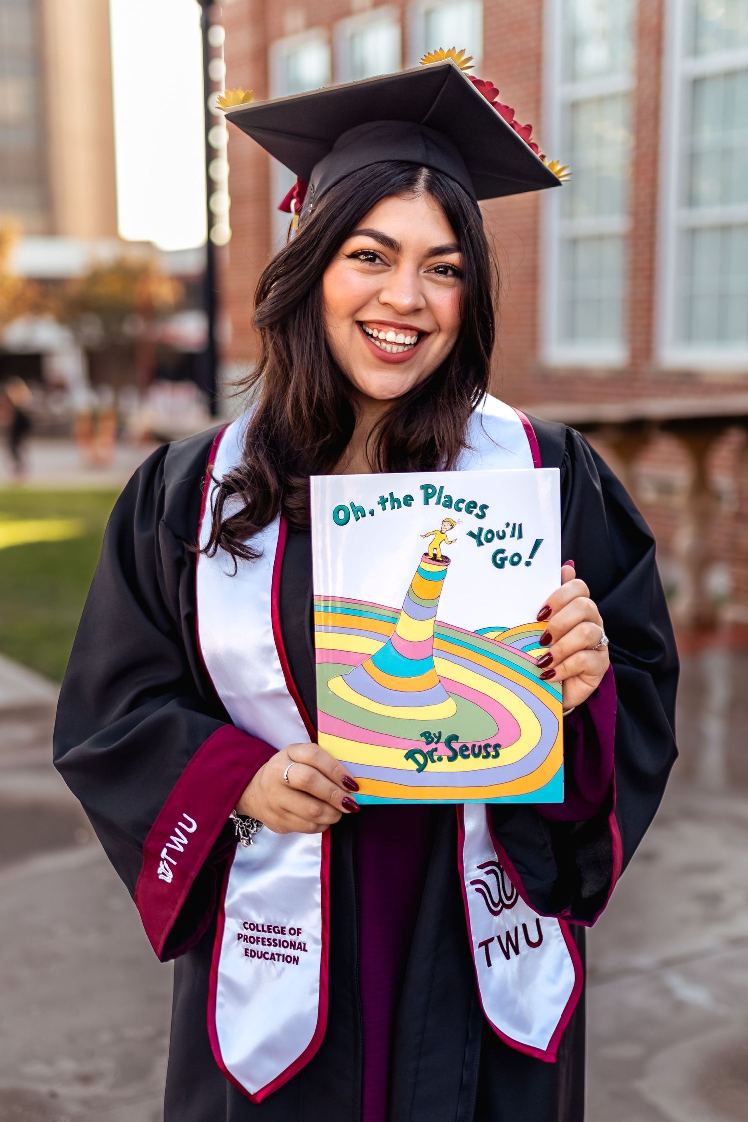 College graduate smiling in cap and gown while holding a decorated graduation cap