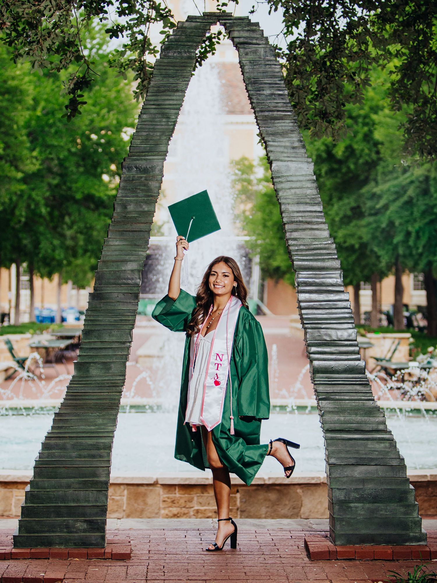 College graduate celebrating outdoors in a green cap and gown