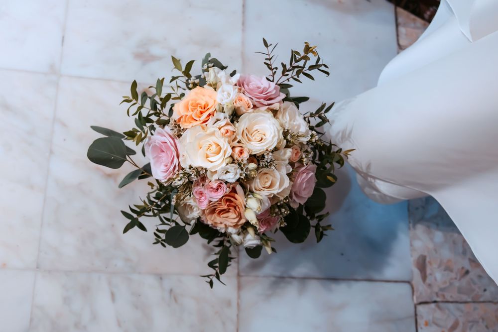 Elegant bridal bouquet with pink, peach, and cream roses with eucalyptus greenery on marble floor.