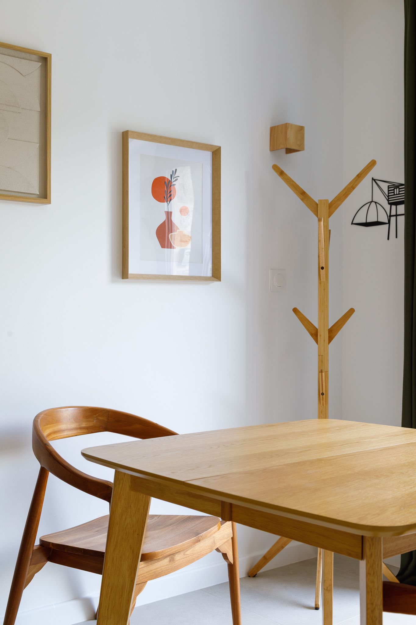 Coin repas minimaliste avec une table en bois clair, une chaise aux lignes courbes, un porte-manteau et des impressions d'art