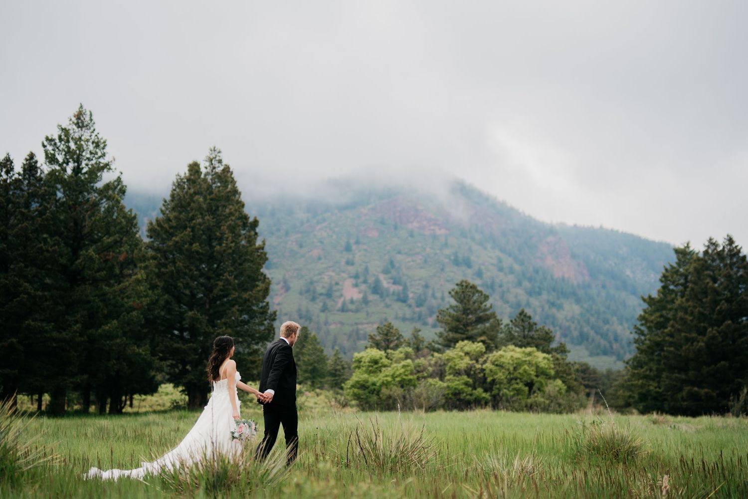 Bride and groom embracing outdoors with lush green hills and ancient ruins in the background on their wedding day.
