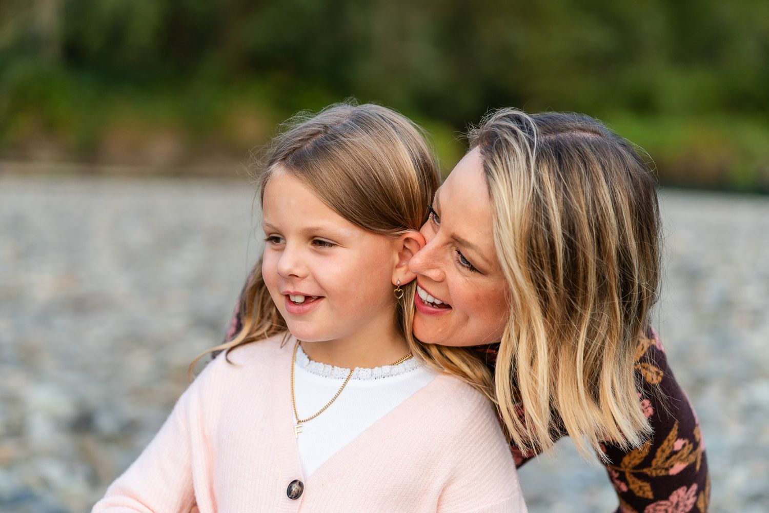 Mom whispering a secret to her smiling daughter.