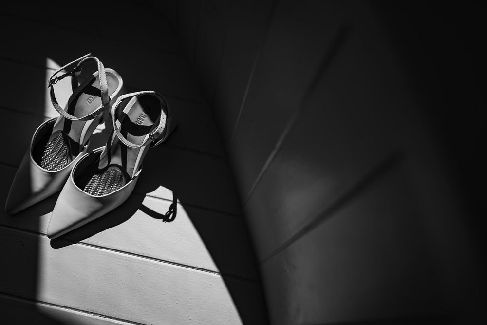 Black and white photo of elegant strappy heels resting on a textured surface with dramatic shadows.