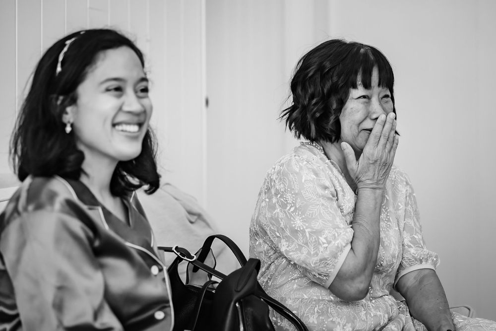 Two women laughing and smiling together in a candid black and white photo at a social gathering.