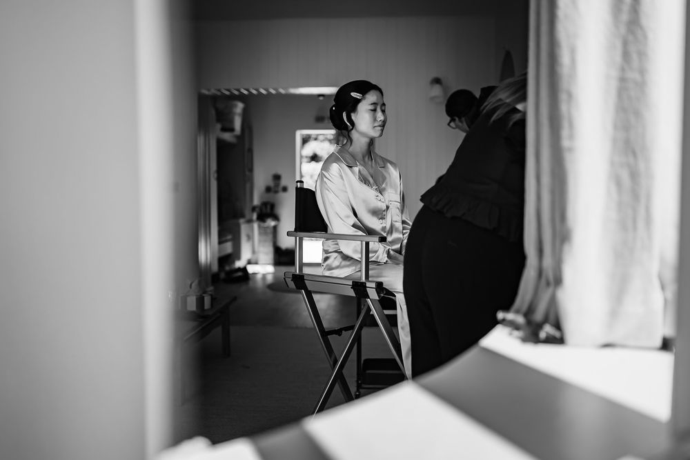 Black and white photo of a bride sitting at a makeup artist station getting ready for her wedding day.
