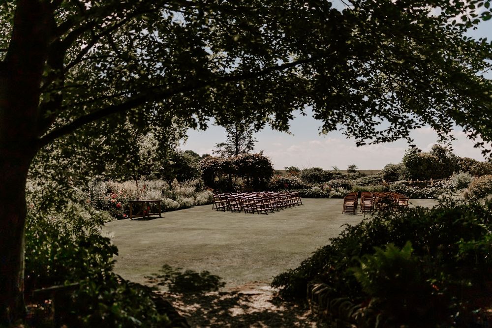 Outdoor wedding ceremony setup with wooden chairs on a green lawn surrounded by lush trees and natural landscaping.