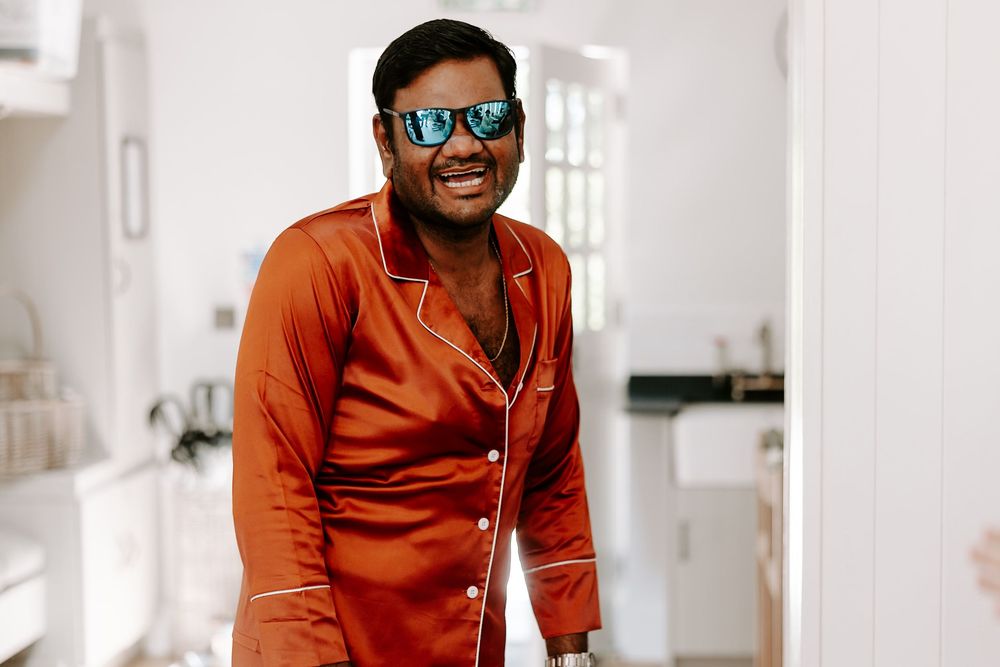 Man in orange satin pajamas and mirrored sunglasses smiling indoors.