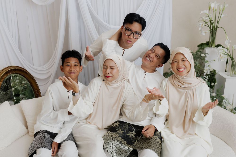 Muslim family in matching white outfits posing together on a sofa with floral decor backdrop.