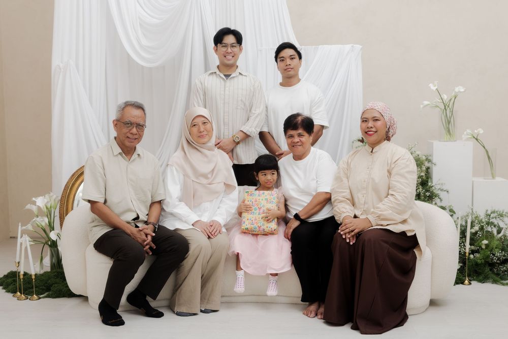 Family portrait of seven people in white and beige outfits posing together in an elegant studio setting.