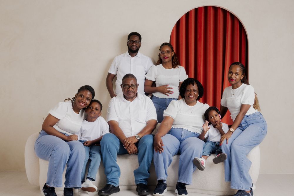 A joyful multigenerational family poses together in matching white tops and blue jeans for a professional portrait.