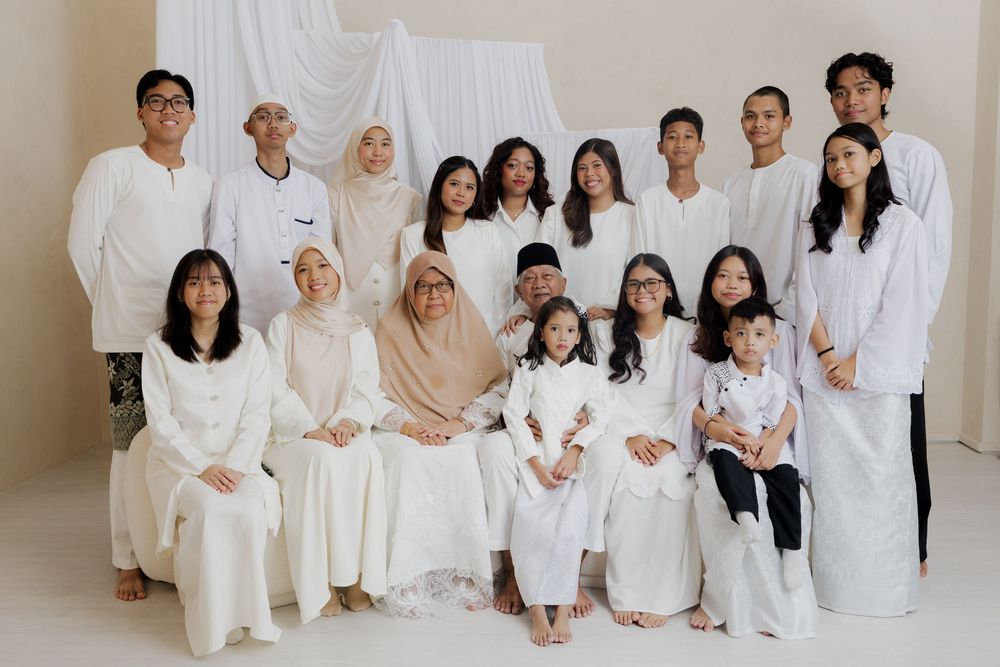 Large Muslim family posing together in matching white outfits for a formal group portrait photo.