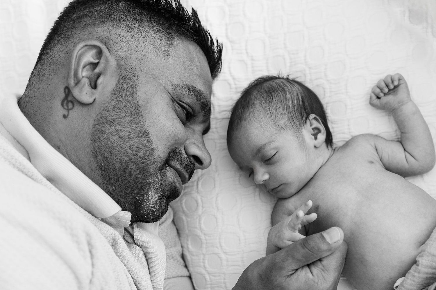 Black and white portrait of a father lying beside his sleeping newborn baby at home