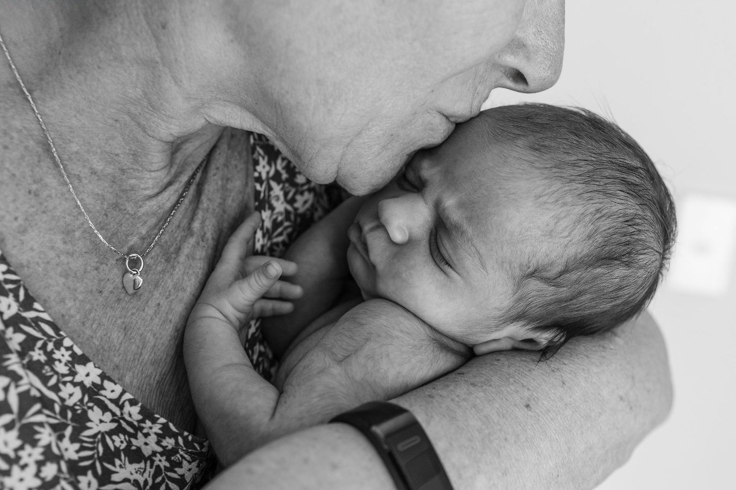 Black and white close-up of a grandmother kissing her newborn granddaughter's head