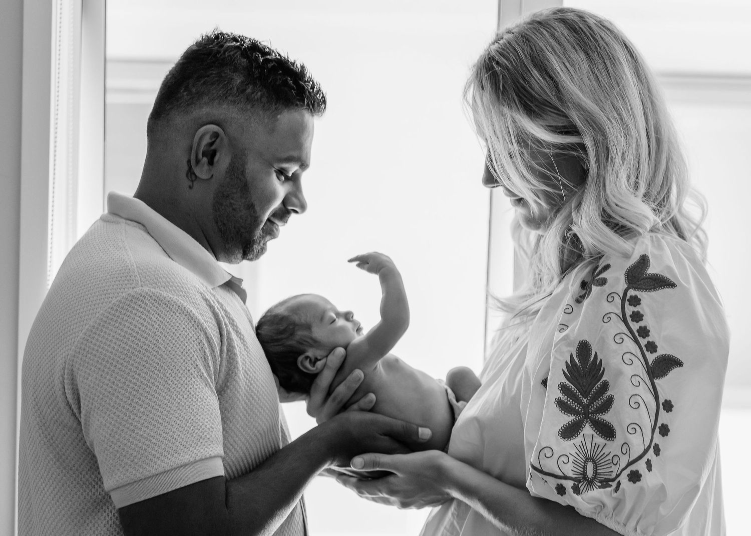 Black and white portrait of a father holding his newborn baby while the mother looks on