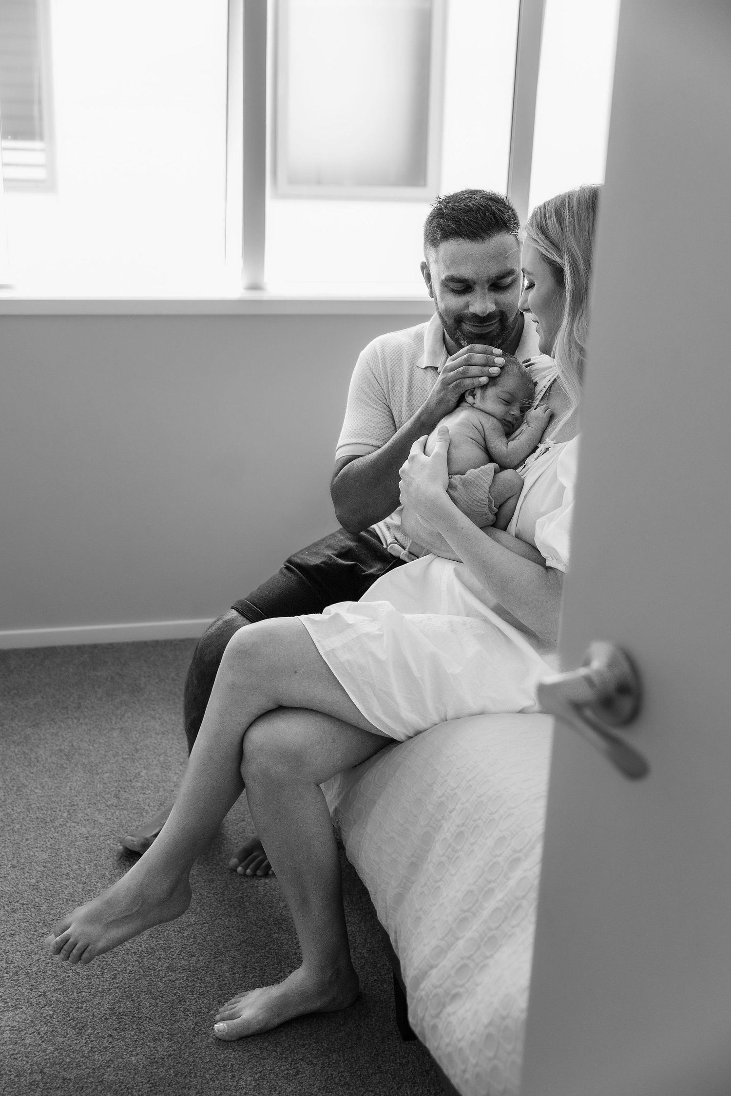 Black and white candid moment of new parents cuddling their baby together at home