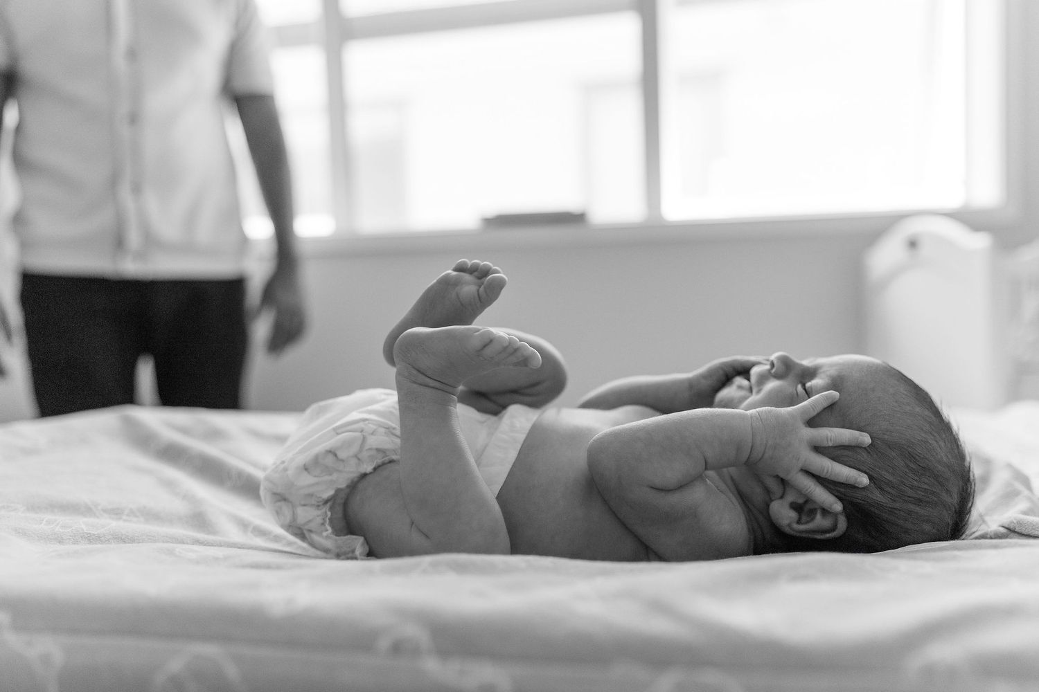Black and white portrait of a newborn baby stretching while lying on a bed at home