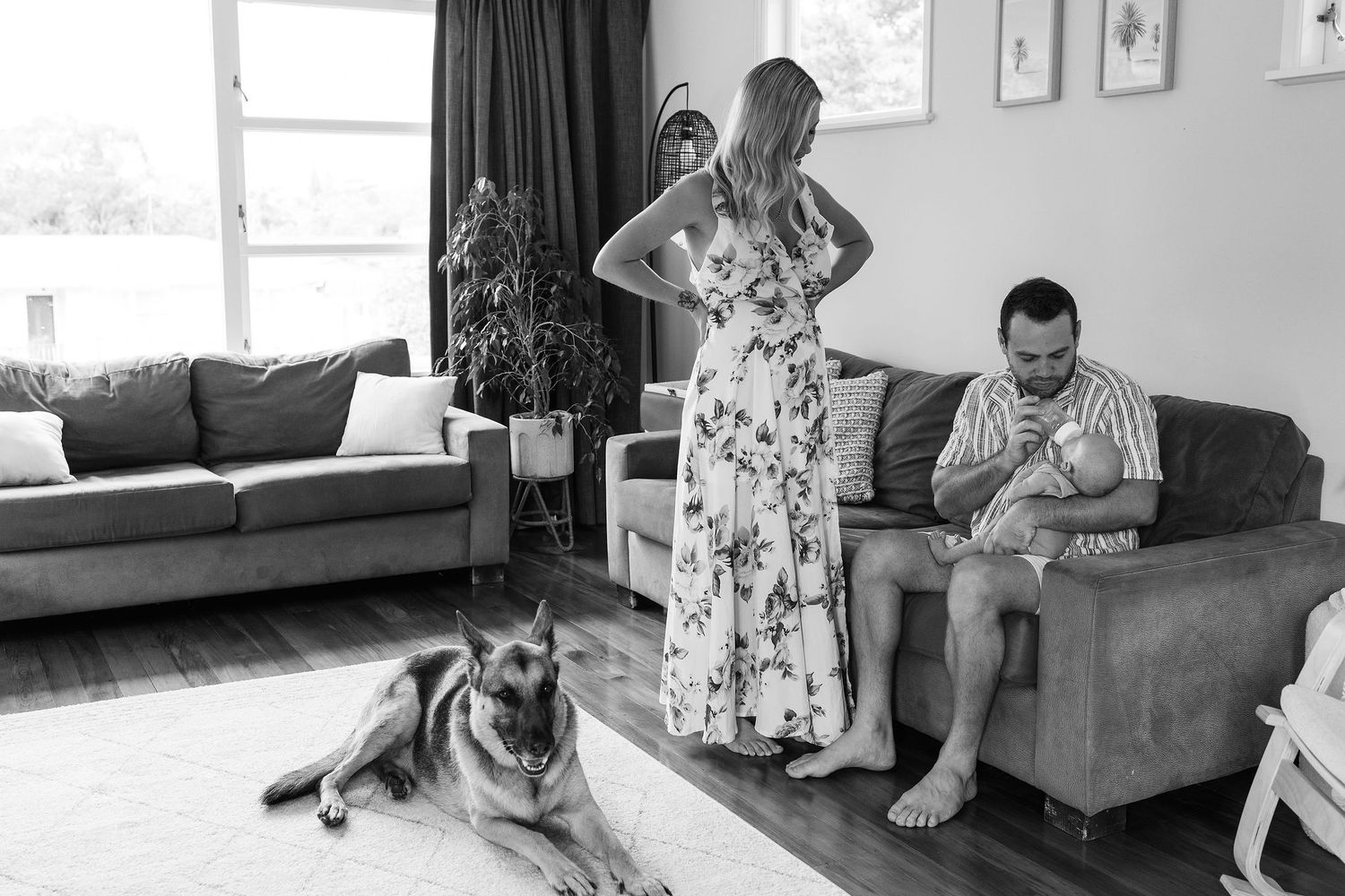 Black and white candid family moment with parents, newborn baby and dog at home