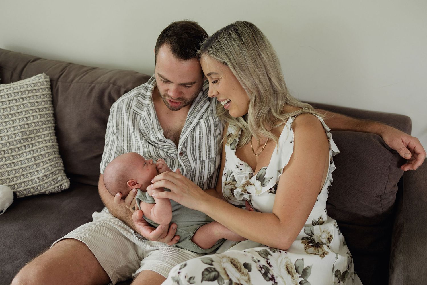 Parents sitting together on the sofa and gently holding their newborn baby