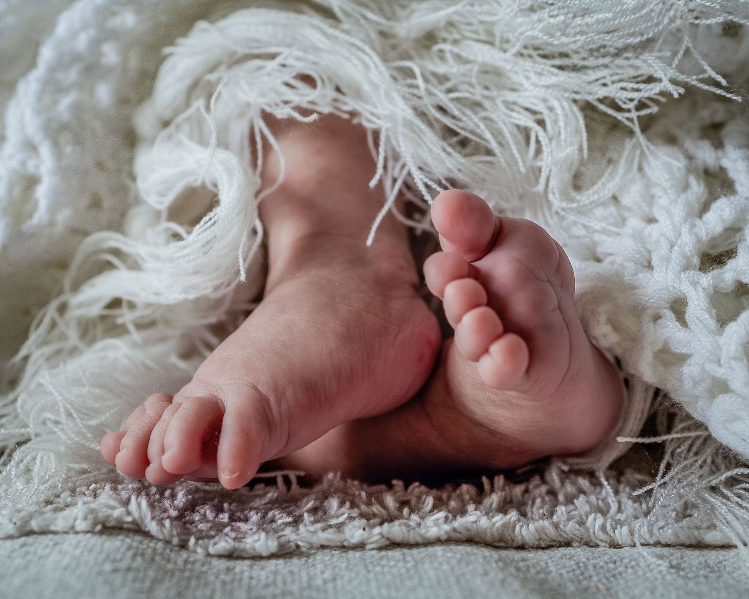 Close-up of a newborn baby’s tiny feet resting on a soft textured blanket
