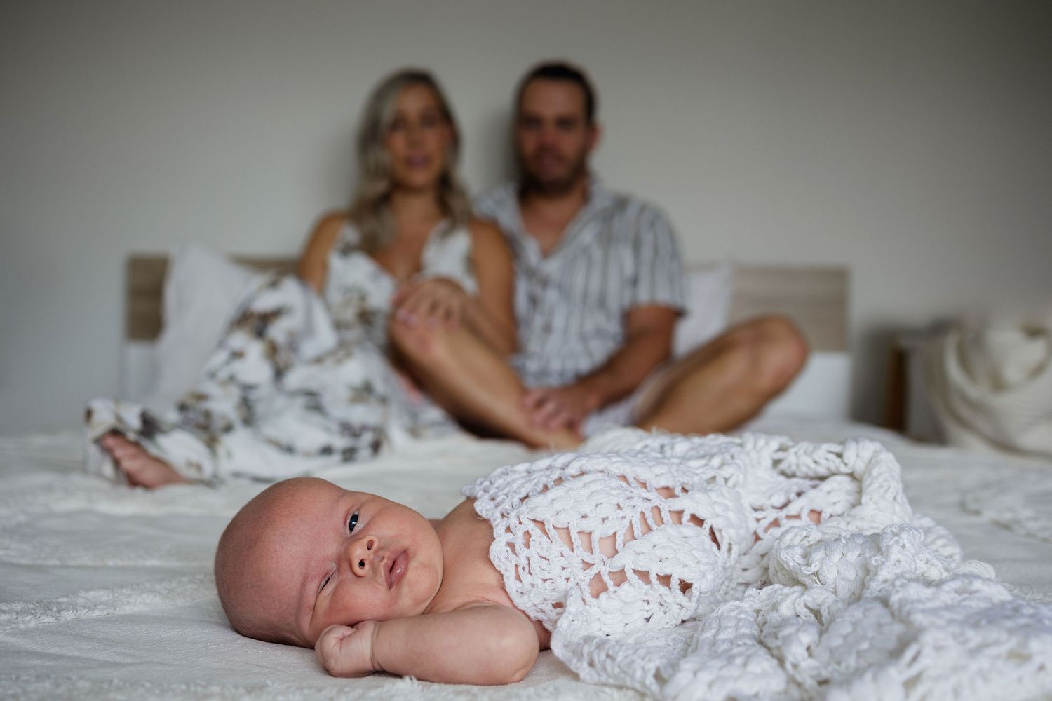 Newborn baby lying in the foreground with parents softly blurred in the background