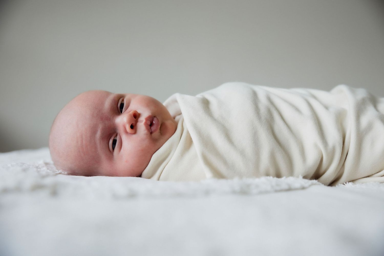 Newborn baby wrapped in a soft cream blanket during a relaxed lifestyle newborn session