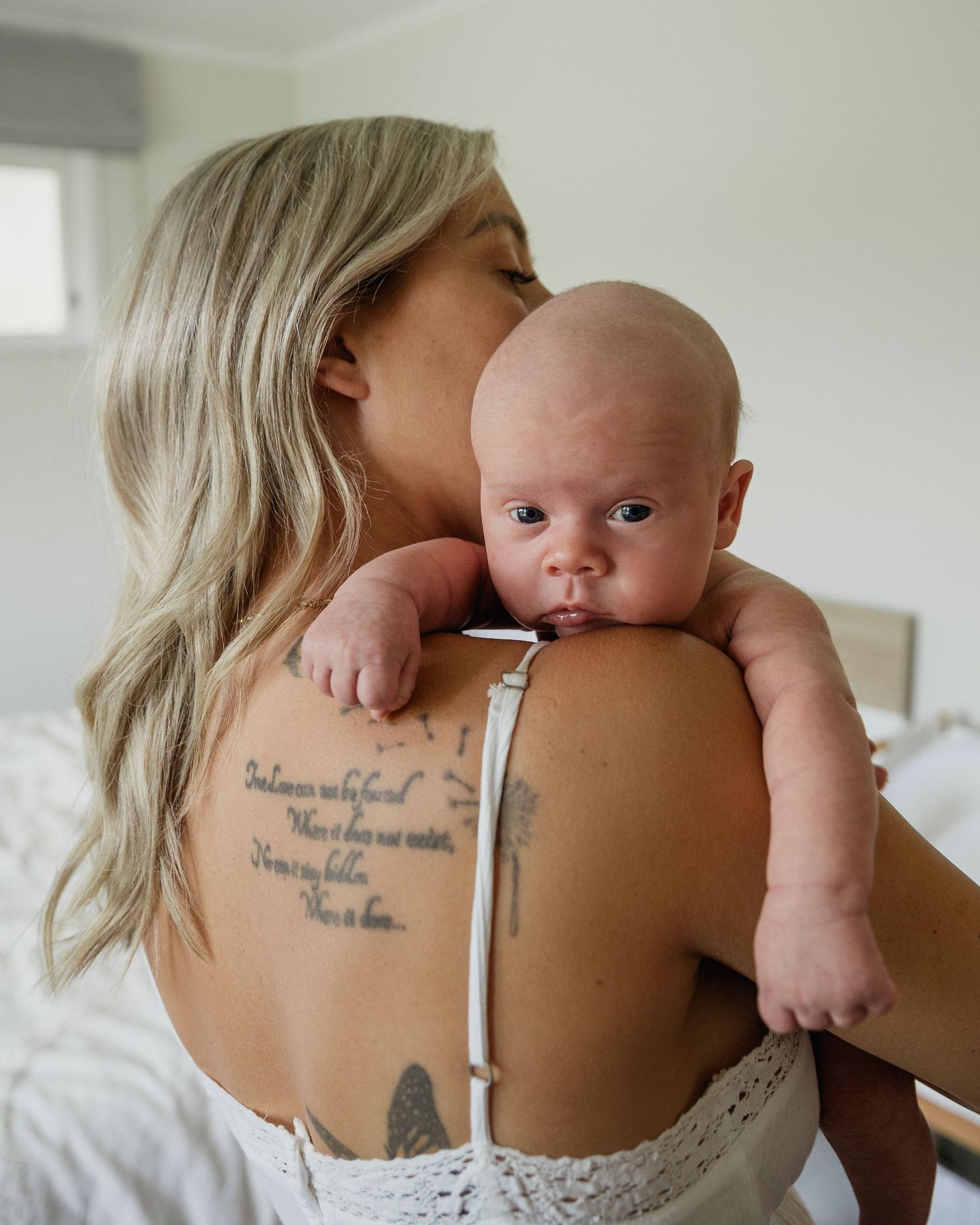 Mother kissing her newborn baby while holding her close during a relaxed in-home session