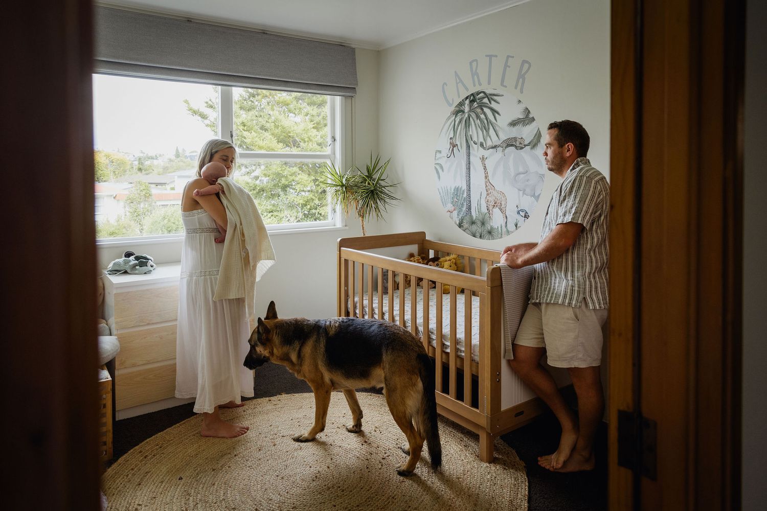 Parents with their newborn baby and dog together in the baby’s nursery at home