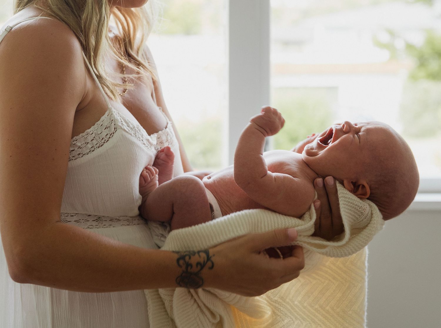 Close-up of a mother gently holding her newborn baby beside a bright window