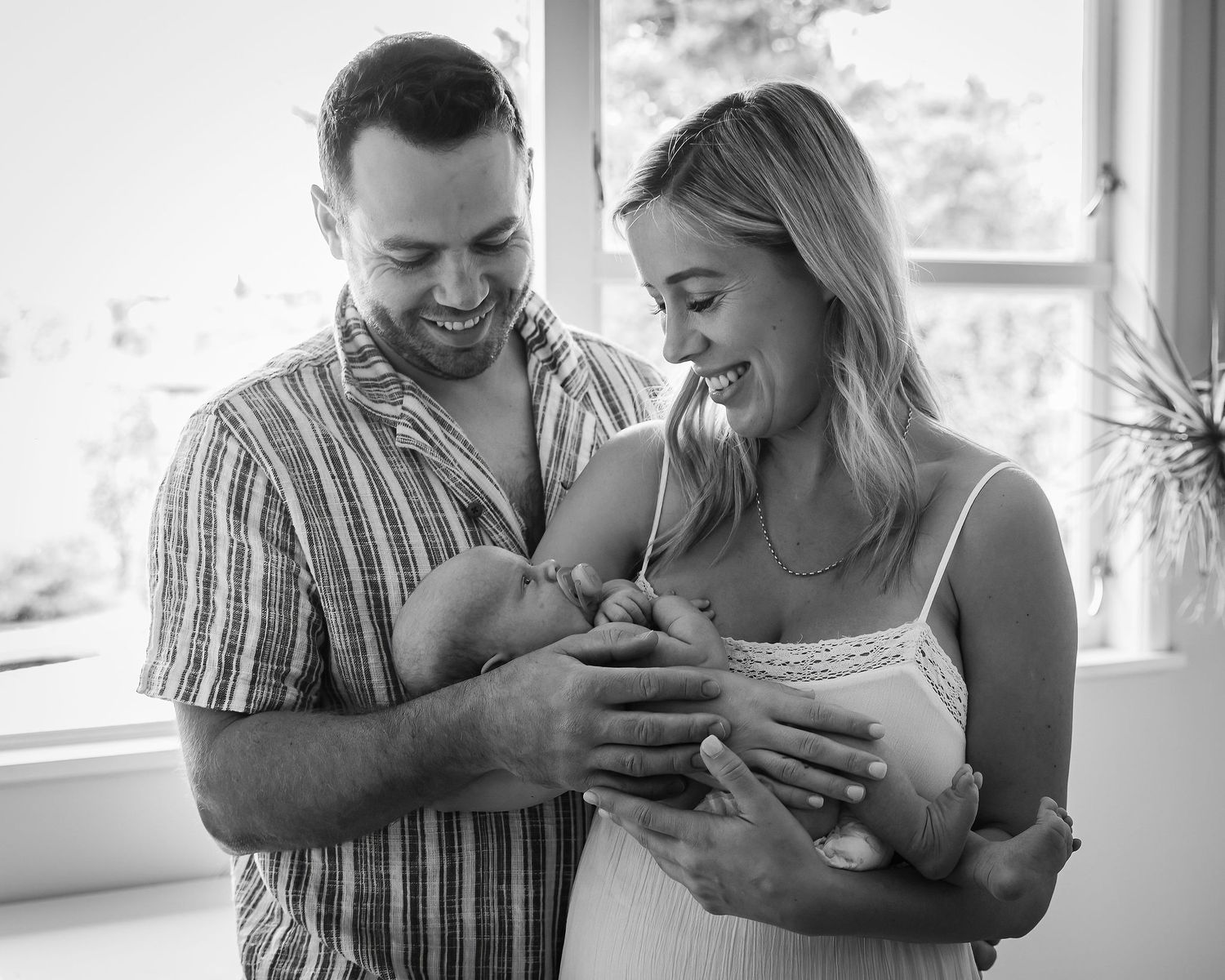 Black and white portrait of new parents standing together while holding their newborn baby