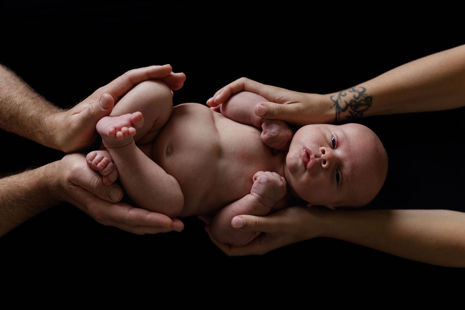 Newborn baby resting safely in a parent’s hands against a dark background