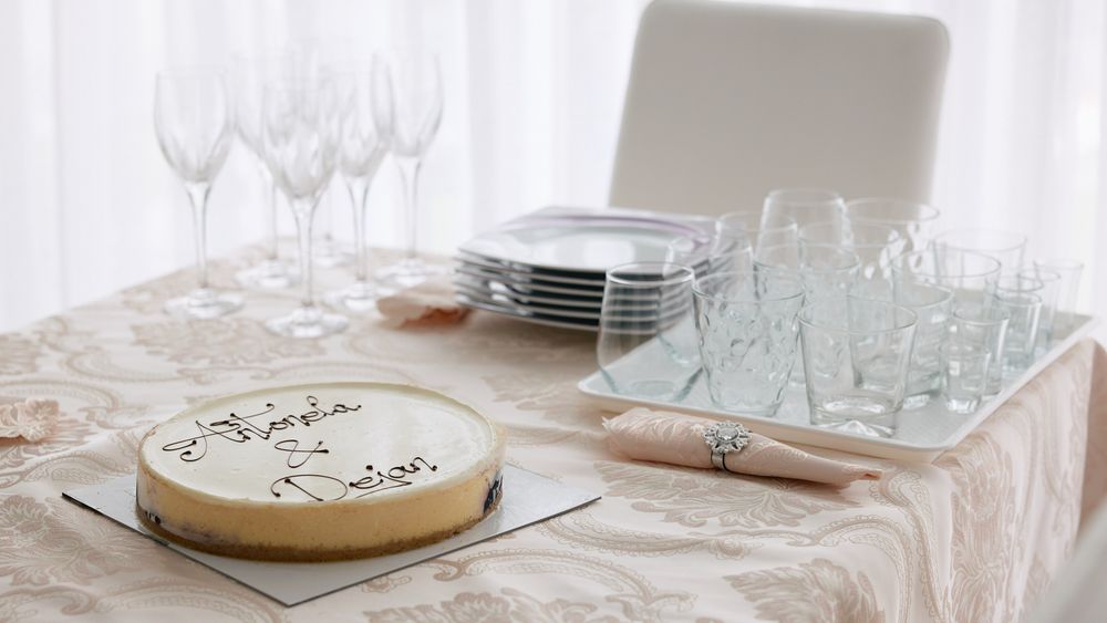 Elegant wedding cake on a table set with champagne flutes, stacked plates, and glassware on a lace tablecloth.