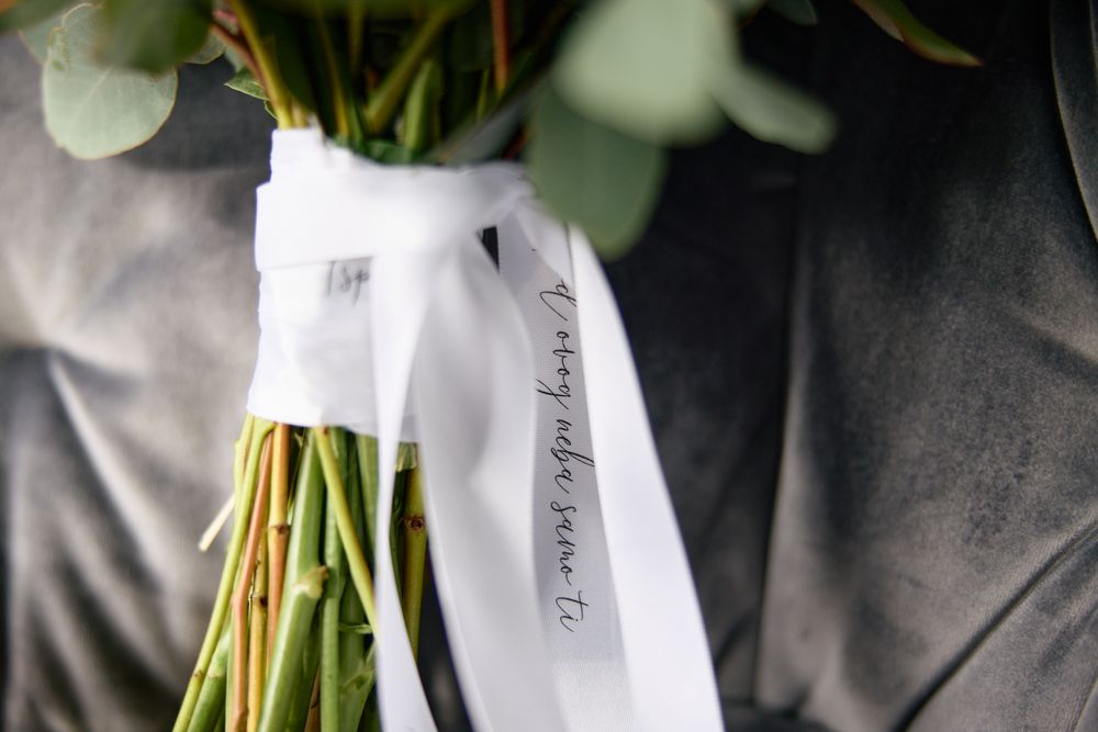 Close-up of a wedding bouquet with green stems tied with a white ribbon featuring elegant calligraphy script.
