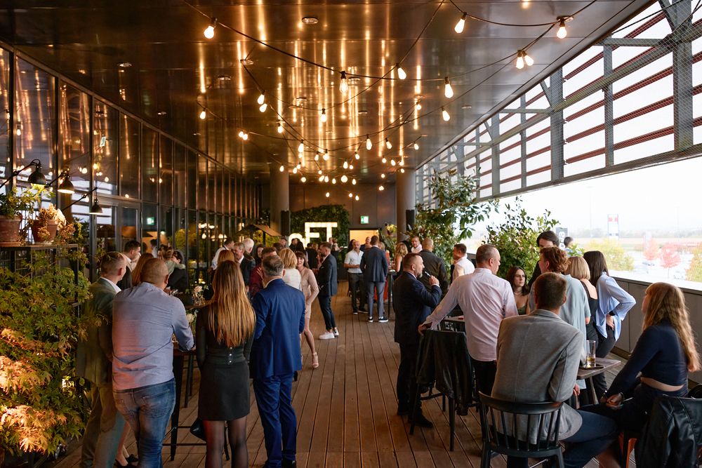 Guests mingle at an elegant rooftop bar venue with warm Edison bulb lighting and lush greenery.