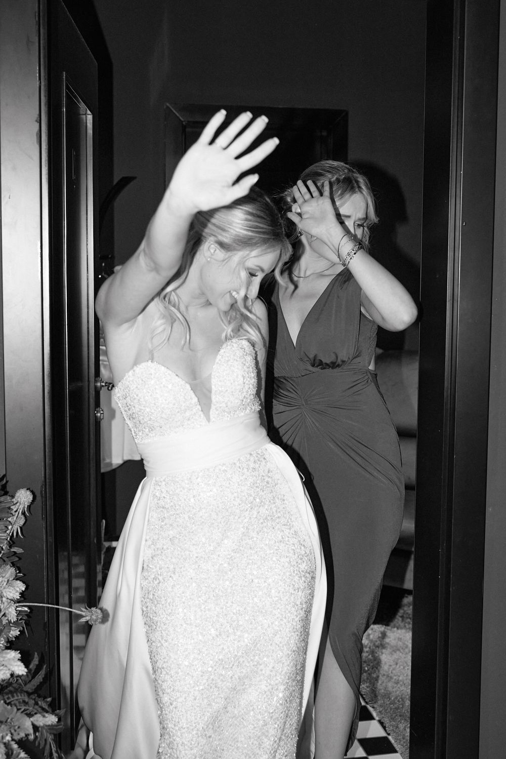 Bride in sparkly wedding gown dancing with bridesmaid in black and white photo.