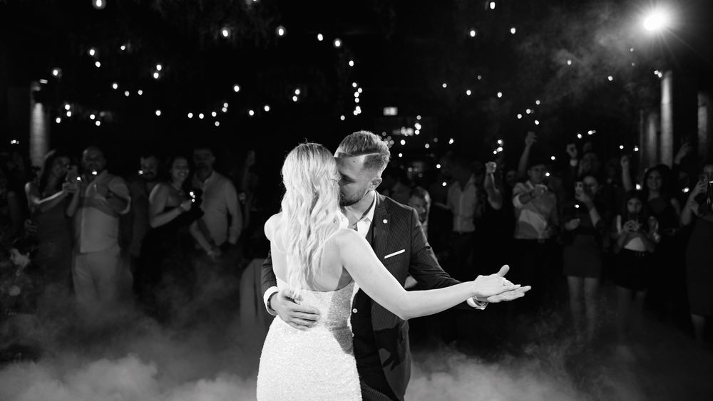 A couple shares their first dance surrounded by guests holding sparklers and dramatic fog at a wedding.