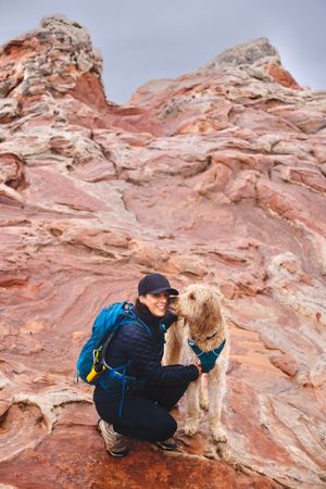 A hiker and golden retriever pause on red sandstone rocks during their outdoor adventure.