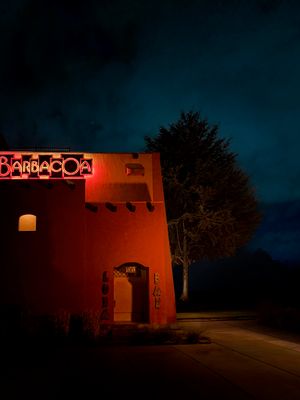 Barbacoa restaurant adobe building glowing with red neon sign at night, Southwestern architecture against dark blue sky.