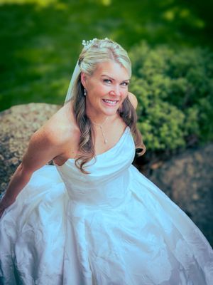 Beautiful bride in elegant white strapless ball gown with floral headpiece smiling outdoors.