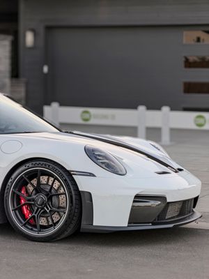 White Porsche 911 GT3 with red brake calipers and black alloy wheels parked on a driveway near a garage.