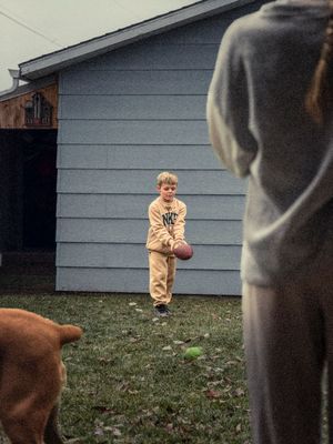Young boy in yellow Nike tracksuit holding football playing in backyard with dog nearby.