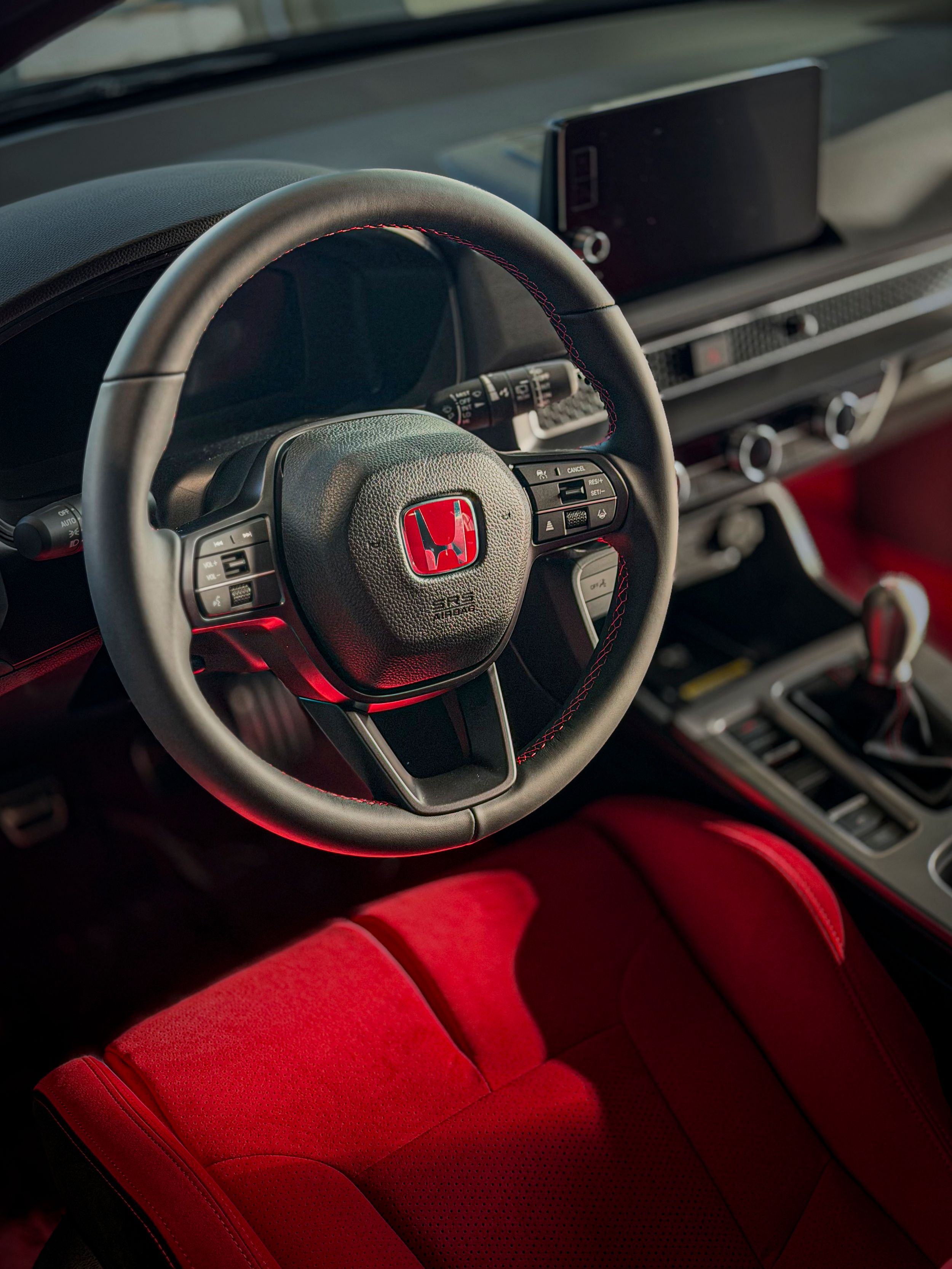 Honda Civic Type R red interior with black steering wheel, red Honda logo, and manual shifter.